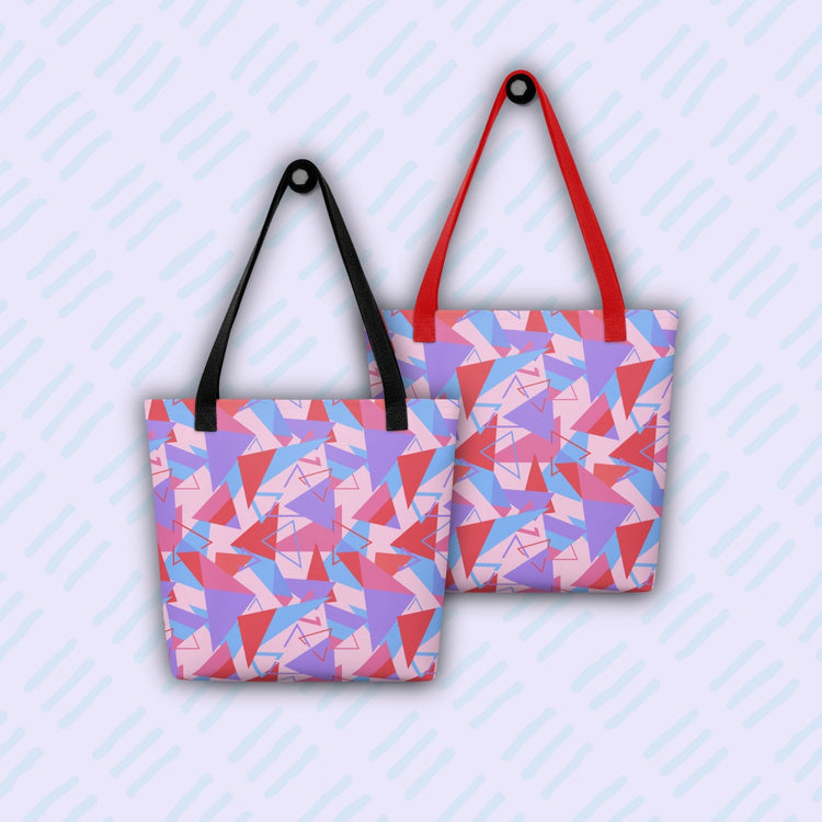 Two Tri the Angle Tote Bags from My Favourite Colour is Rainbow, with geometric patterns in red, pink, and purple on a light backdrop, are displayed. Crafted from durable polyester with red and black straps, they're are shown against a pastel background.