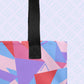 A close-up of the spacious Tri the Angle Tote Bag by My Favourite Colour is Rainbow shows its colourful geometric shapes in pink, purple, red, and blue. It features a black handle and is set against a light background.