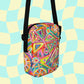 The Tropical Geometry Mini Crossbody Bag by My Favourite Colour is Rainbow showcases colorful triangles and circles in red, pink, green, and yellow. It features a black strap for hands-free use and stands out against a light blue and cream checkered background.