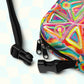 Close-up of the Tropical Geometry Mini Crossbody Bag by My Favourite Colour is Rainbow, showcasing abstract triangles and circles. Black zippers and adjustable straps provide convenience, set against a light blue and white checkered backdrop for added vibrancy.