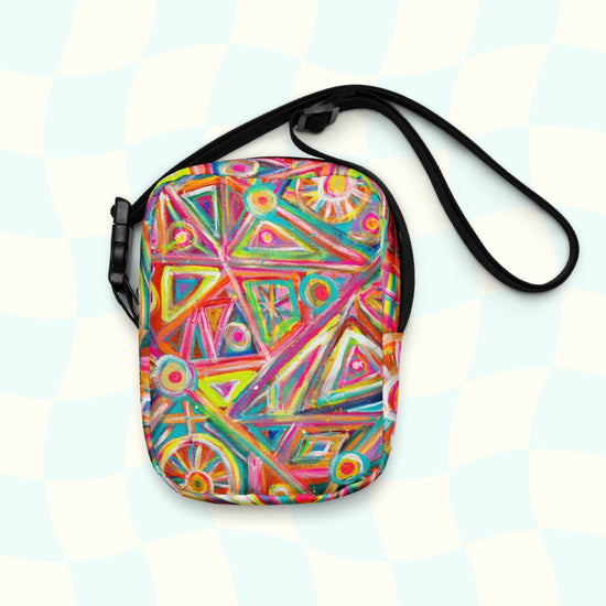 Experience hands-free convenience with the Tropical Geometry Mini Crossbody Bag by My Favourite Colour is Rainbow, featuring a lively abstract print of red, orange, pink, green, and blue geometric shapes like triangles and circles on a light checkered background.