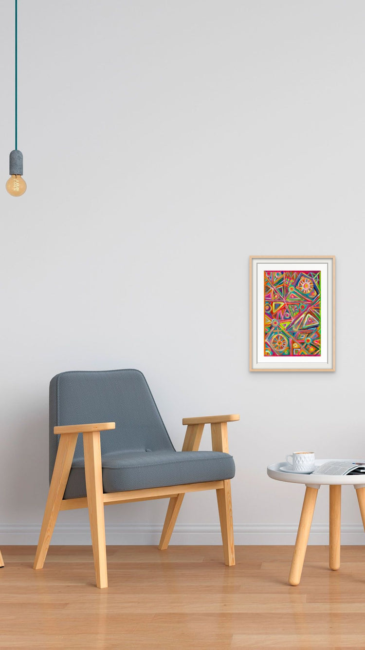 A minimalist room features a wooden armchair, a round table on a light wood floor, and My Stores Tropical Geometry Fine Art Print on the white wall. A ceiling lamp with an exposed bulb lights up a cup and book resting on the table, enhancing the serene ambiance.