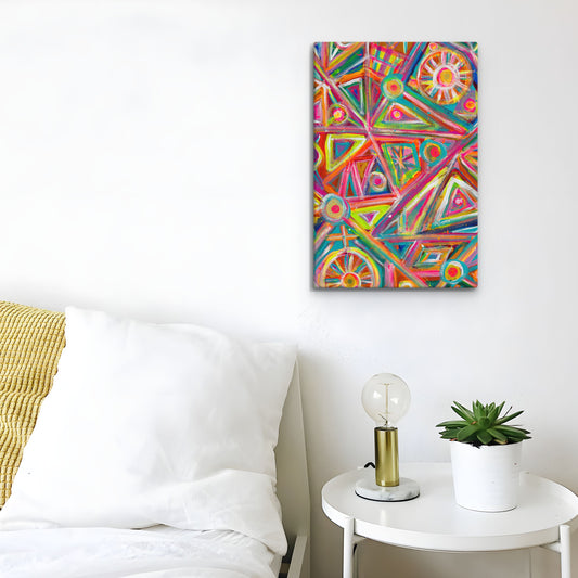 A colorful Tropical Geometry Canvas Artwork by My Favourite Colour is Rainbow hangs on a white wall above a cozy bed with white bedding and a yellow pillow. A round white side table beside the bed holds a modern lamp and a small potted plant.