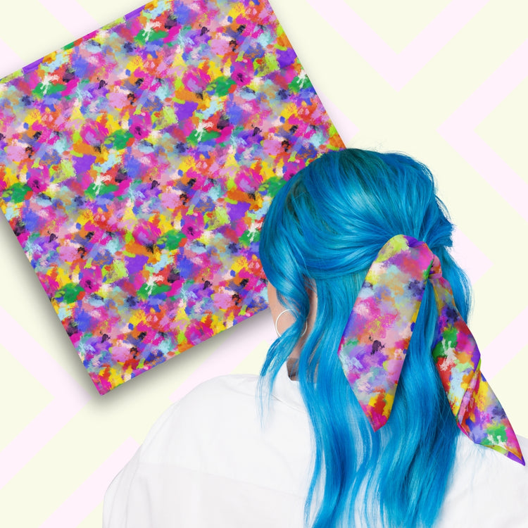 Two views of the 'Watercolour Rainbow' Bandana by My Favourite Colour is Rainbow.  At top left, a flat lay of the bandana.  At bottom right, a person with vibrant blue hair is seen from behind, wearing the bandana in her hair.  The bandana features a vibrant abstract design with blue, green, pink, orange, and purple splashes. 
