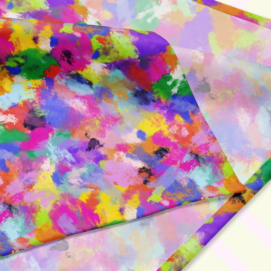 A closeup of the 'Watercolour Rainbow' Bandana by My Favourite Colour is Rainbow featuring a vibrant abstract design with blue, green, pink, orange, and purple splashes. The design is printed on only one side of the bandana.
