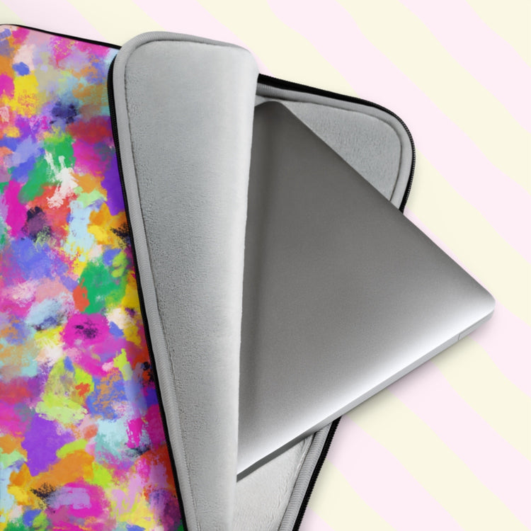 A close-up of a silver laptop partially out of the Watercolour Rainbow Laptop Sleeve by My Favourite Colour is Rainbow, showcasing its vibrant abstract pattern with pink, purple, blue, yellow, and green splashes of colour.  It has a grey padded interior to keep your laptop safe from scratches.  The print is on only one side of the laptop sleeve, the other side is black. It is shown on a pastel background.
