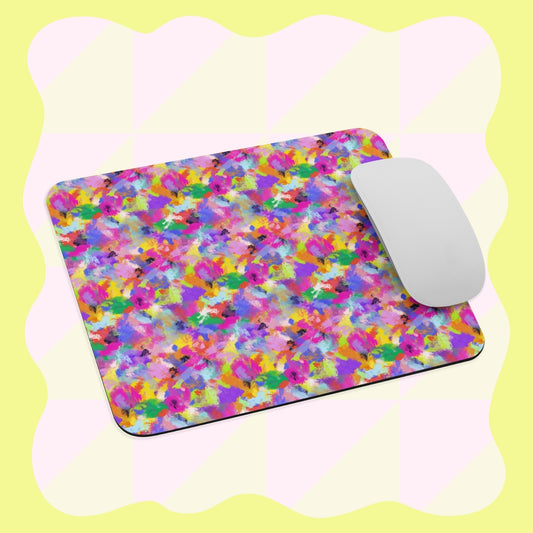 A white computer mouse rests on the Watercolour Rainbow Mouse Pad by My Favourite Colour is Rainbow, featuring an abstract multicolored paint splatter design, set against a light yellow background with soft wavy patterns.