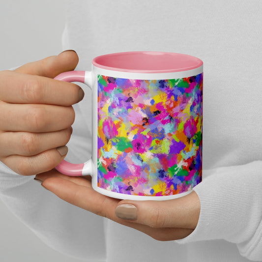 A person holds the Watercolour Rainbow Mug by My Favourite Colour is Rainbow, showcasing vibrant abstract splashes of pink, purple, blue, green, and yellow. Its interior and handle are pink. They wear a white top with light-colored nail polish.