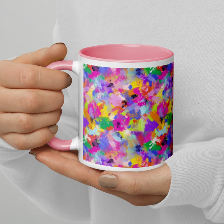 A person holds the Watercolour Rainbow Mug by My Favourite Colour is Rainbow, showcasing vibrant abstract splashes of pink, purple, blue, green, and yellow. Its interior and handle are pink. They wear a white top with light-colored nail polish.