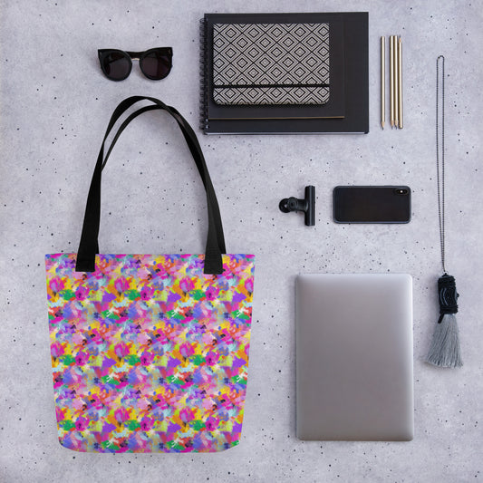 A flat lay on a gray surface includes sunglasses, notebooks, pens, a smartphone, laptop, tassel keychain, clip, and a Watercolour Rainbow Tote Bag by My Favourite Colour is Rainbow featuring dual black handles.