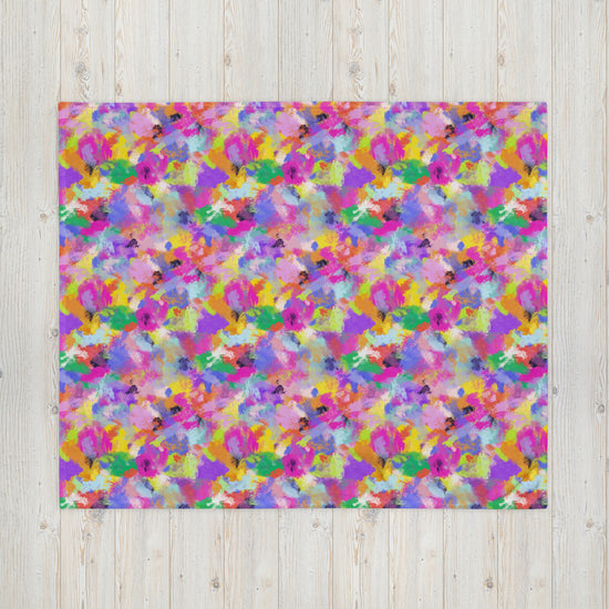 An abstract painting, akin to My Favourite Colour is Rainbows Watercolour Rainbow Throw Blanket, showcases vivid pink, purple, yellow, green, and blue splashes against a light wooden background.