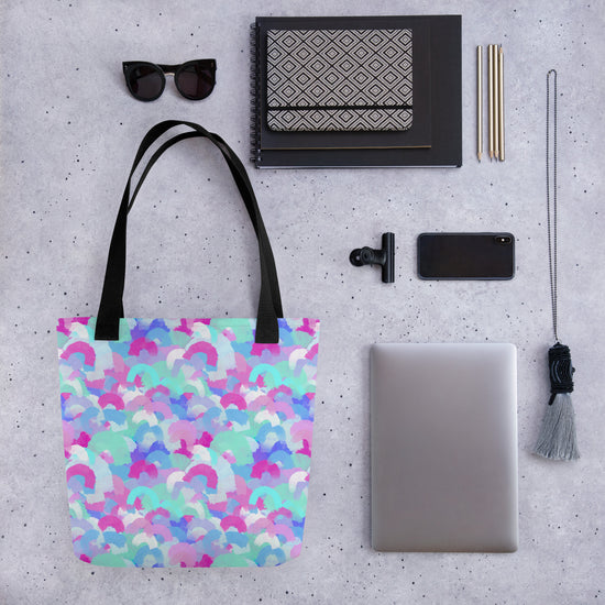 The Pastel Rainbow Tote Bag by My Favourite Colour is Rainbow is the centerpiece of a flat lay, surrounded by sunglasses, notebooks, pens, a phone, a camera lens attachment, a closed laptop, a woven pouch, and a tassel keychain.